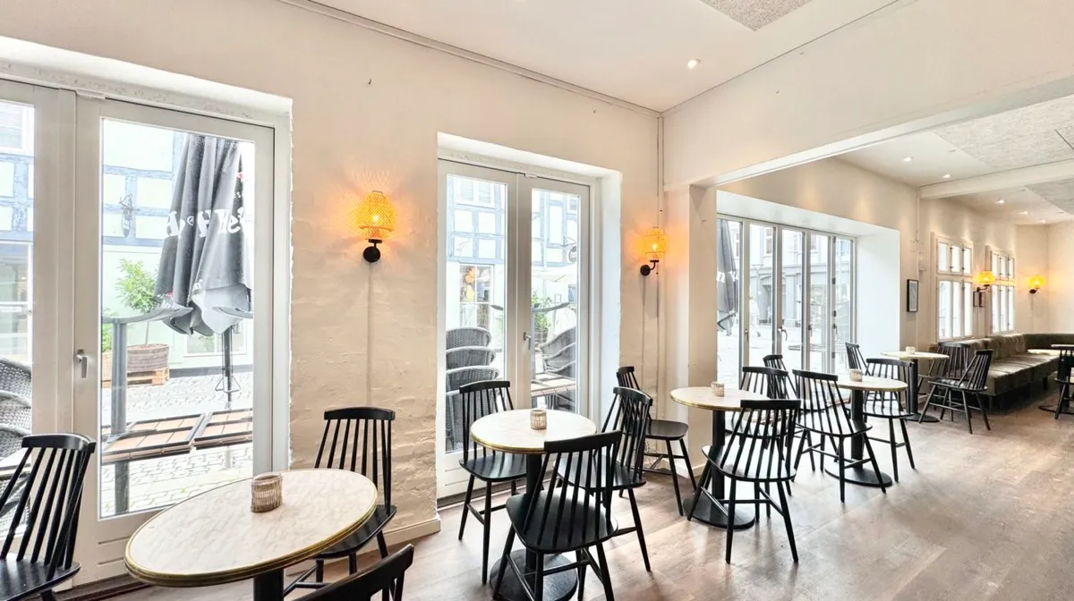 En stor, moderne restaurant med høje vinduer, lyse og hyggelige borde, og en indretning med en neutral farvetone