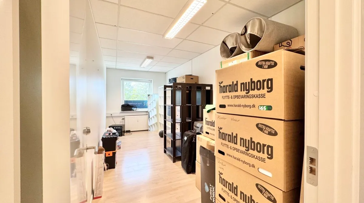 Foto af lokaler med møbler og bokse samt vinduer og døre, der er forsynet med tekst