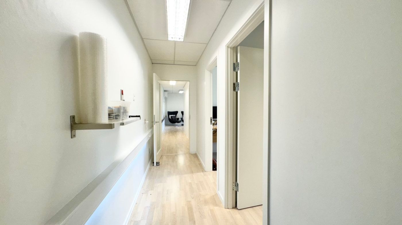 Et tomt og lyse kontor i en hvid og træfarvet indretning med åbne døre og udstyr på væggen