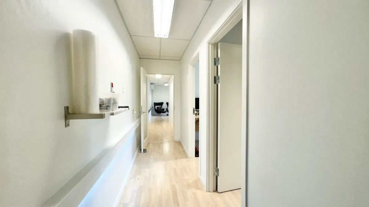 Et tomt og lyse kontor i en hvid og træfarvet indretning med åbne døre og udstyr på væggen