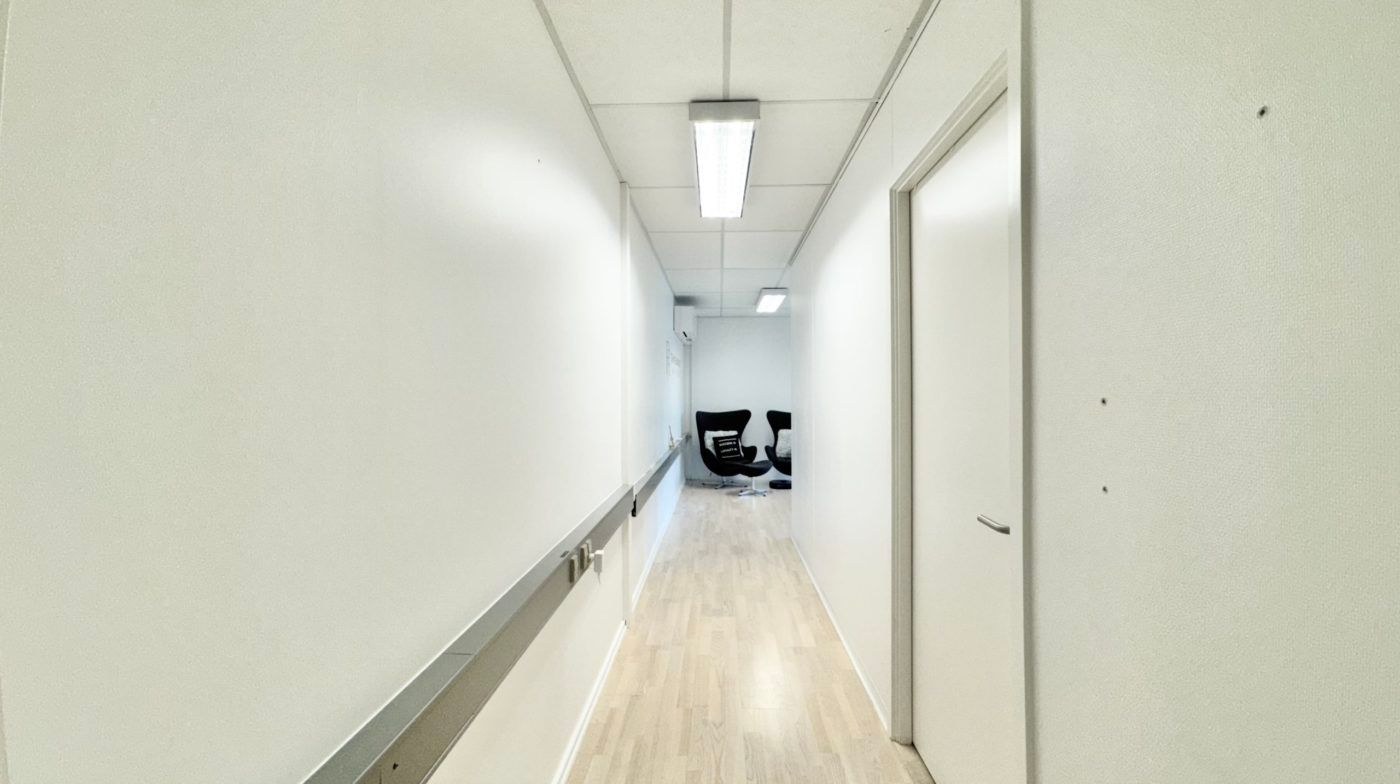 Hallen er delvist møblet med to stole og en stol med pude samt et hvidt dørblad og hvidt vægpanel.