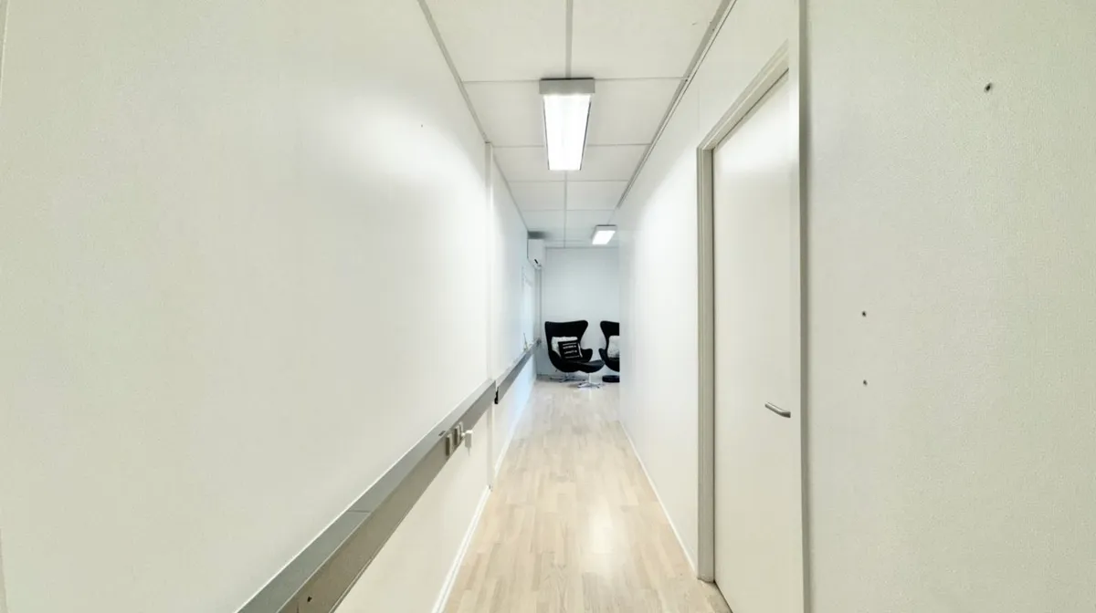 Hallen er delvist møblet med to stole og en stol med pude samt et hvidt dørblad og hvidt vægpanel.