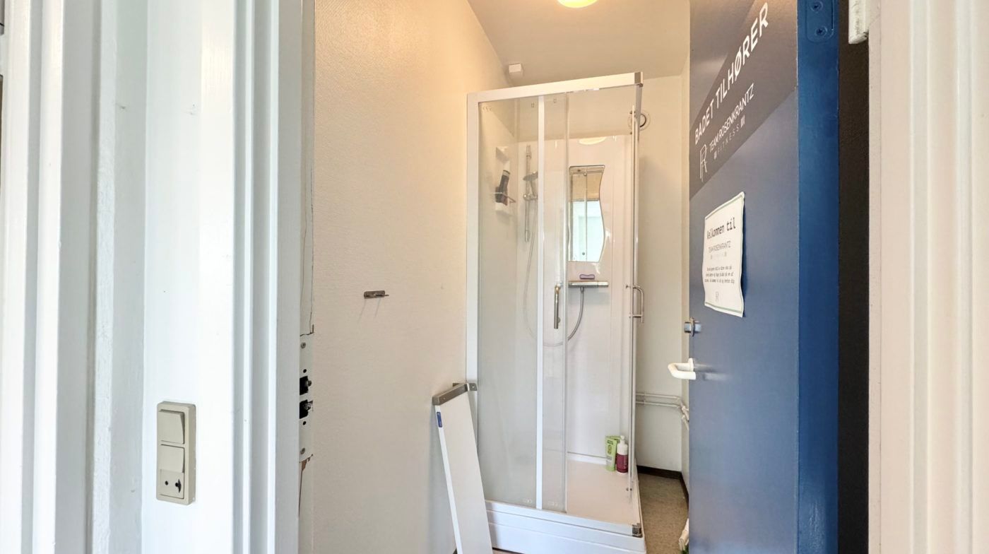 Et moderne badeværelse med en hvid bruser og håndklædeholder, en dør og en væg med et skilt og en indgang til et