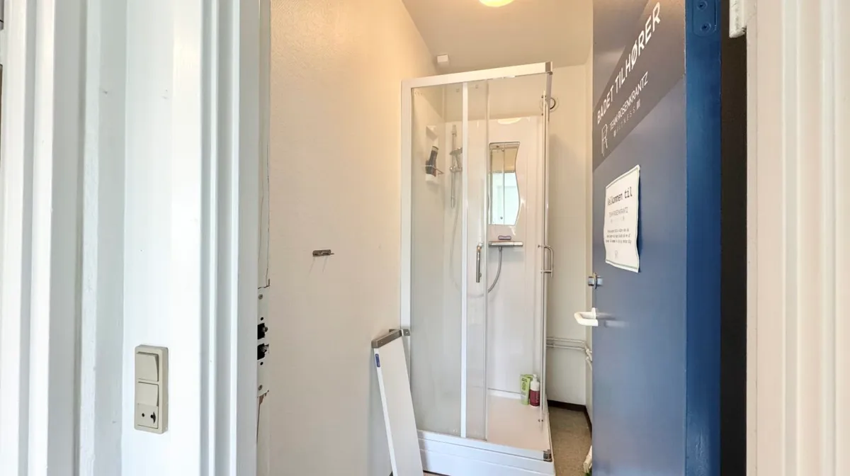 Et moderne badeværelse med en hvid bruser og håndklædeholder, en dør og en væg med et skilt og en indgang til et