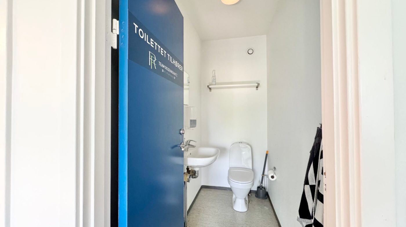 Et lille toiletrum med en hvid toilet og et hvidt vaskebækken, der er installeret i hjørnet af rummet.