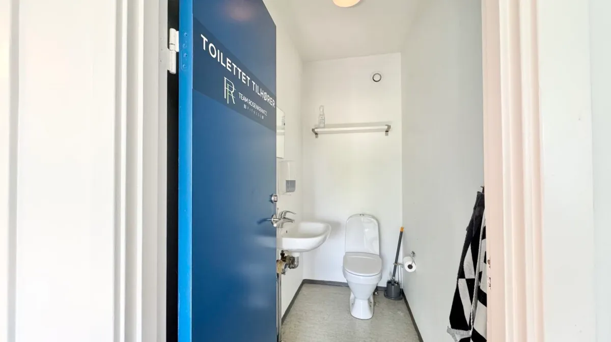 Et lille toiletrum med en hvid toilet og et hvidt vaskebækken, der er installeret i hjørnet af rummet.