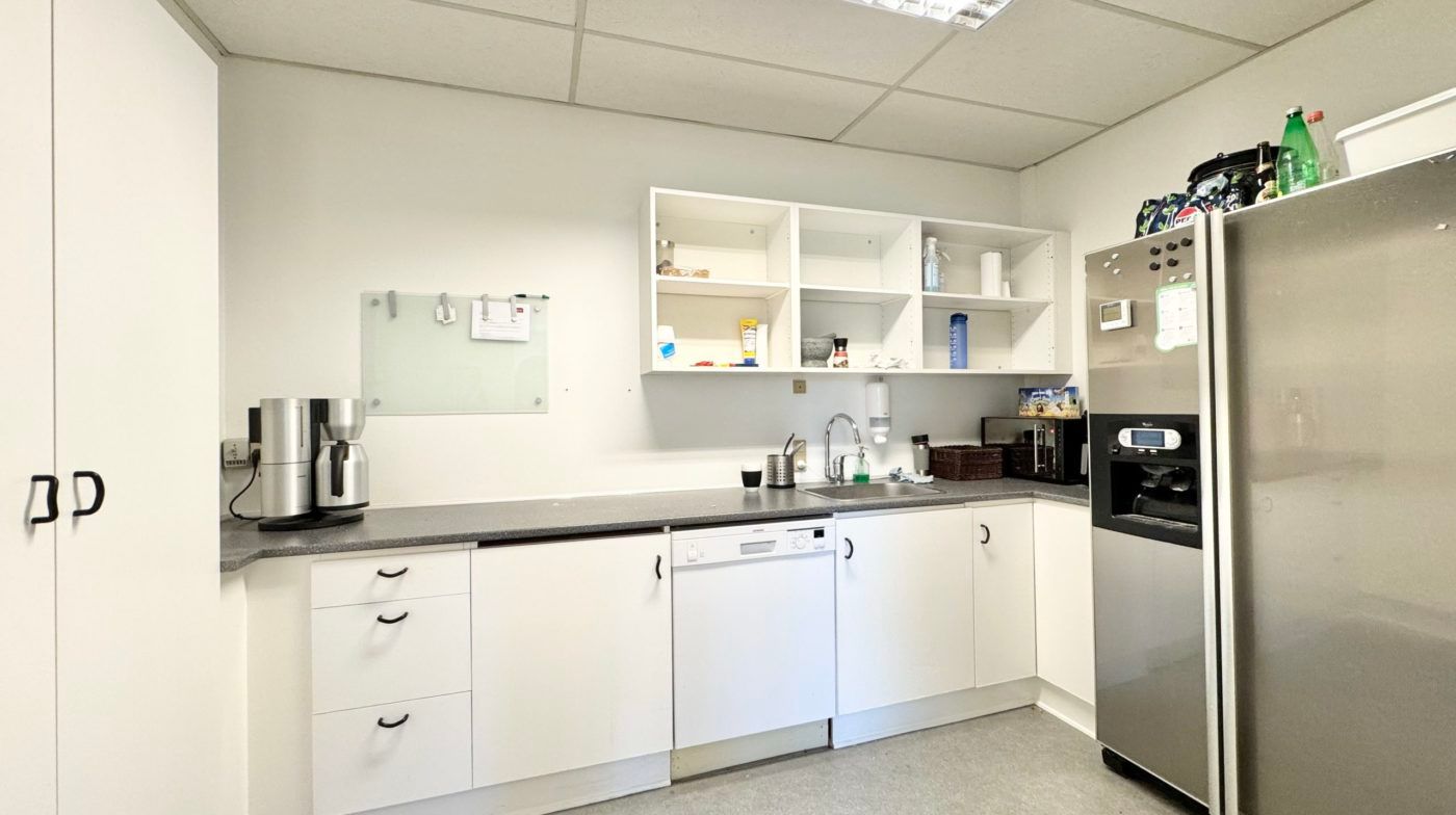 En funktionel køkkendel med en mikrobølgeovn, køleskab, vaskemaskine, ekspreskaffemaskine, kogeplade, væskevask og