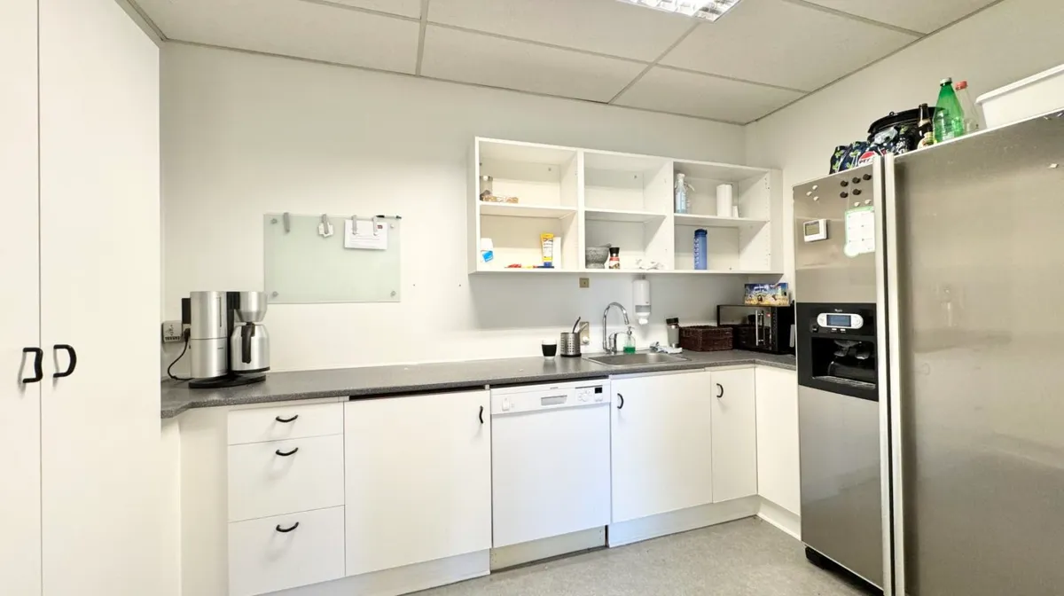 En funktionel køkkendel med en mikrobølgeovn, køleskab, vaskemaskine, ekspreskaffemaskine, kogeplade, væskevask og