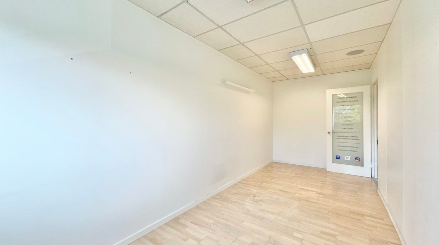 En tom kontorrum med hvide vægge og lysegule gulvbelægning samt to indbygget lysekroner og en dør med et tekstskilt