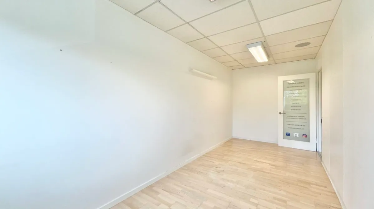 En tom kontorrum med hvide vægge og lysegule gulvbelægning samt to indbygget lysekroner og en dør med et tekstskilt