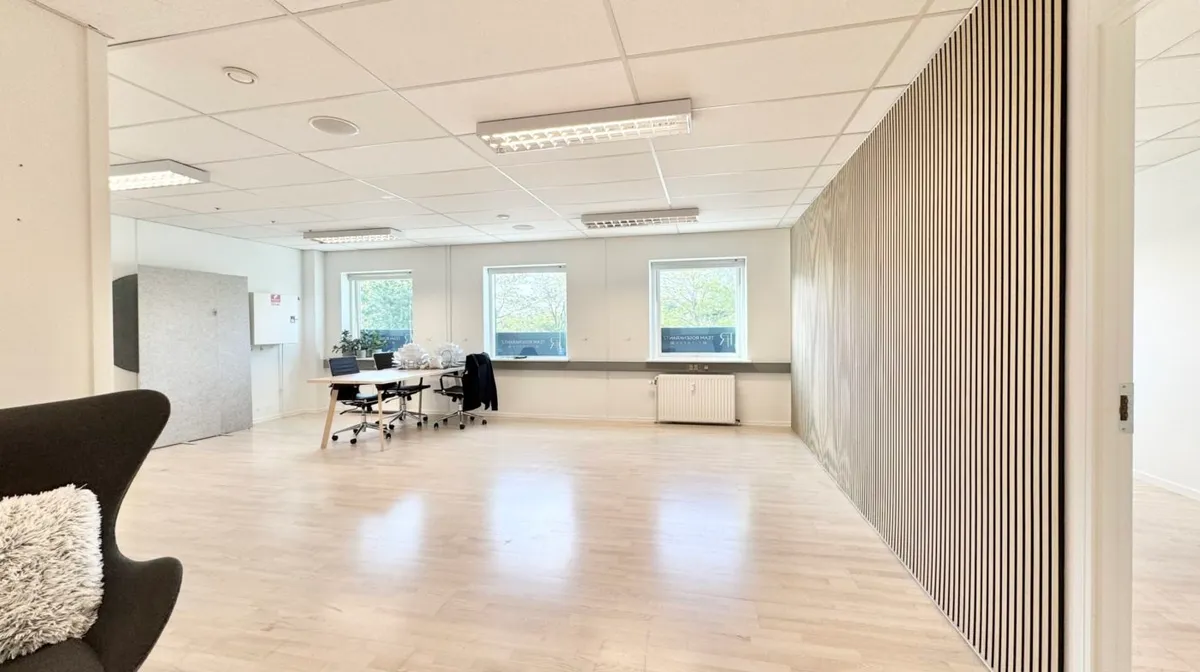 Kontor med masser af lys og plads til møder. Bord og stole i en afdelingen, og tavle med hvidt papir i den anden. Høj