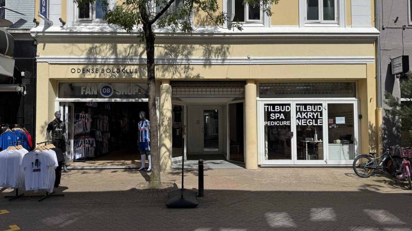 Kvindemanequin i OB-trøje og to hanemanequins i OB-skjorte foran fanbutik. Spa- og pedicure-lokal med mange vinduer og