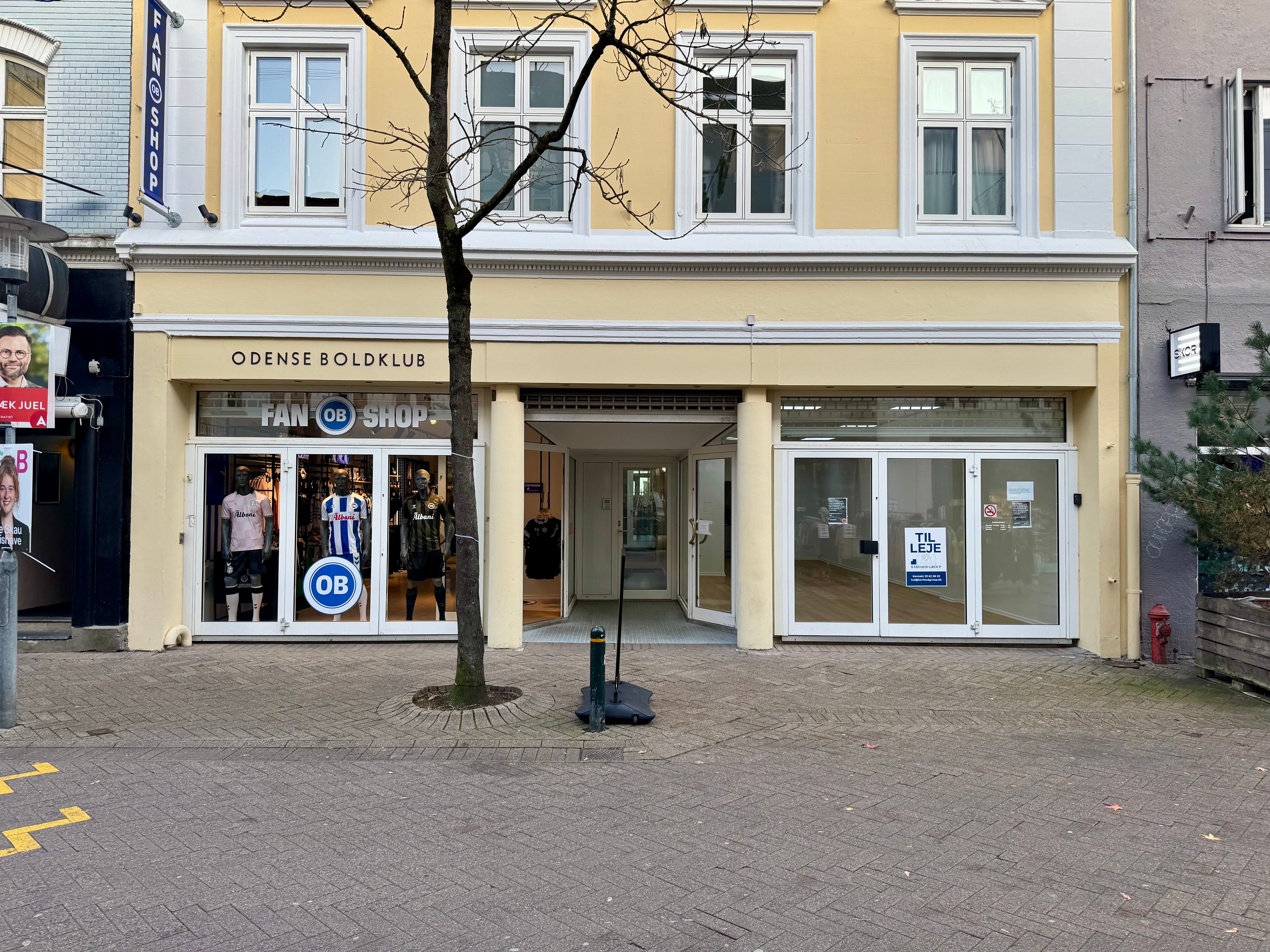 Butikslokal til leje på Kongensgade 39, Odense C. Lokale med vinduer, skilte med Odense Boldklub og OB-shop, glasdøre og tydelig vejledning til åbningstider.