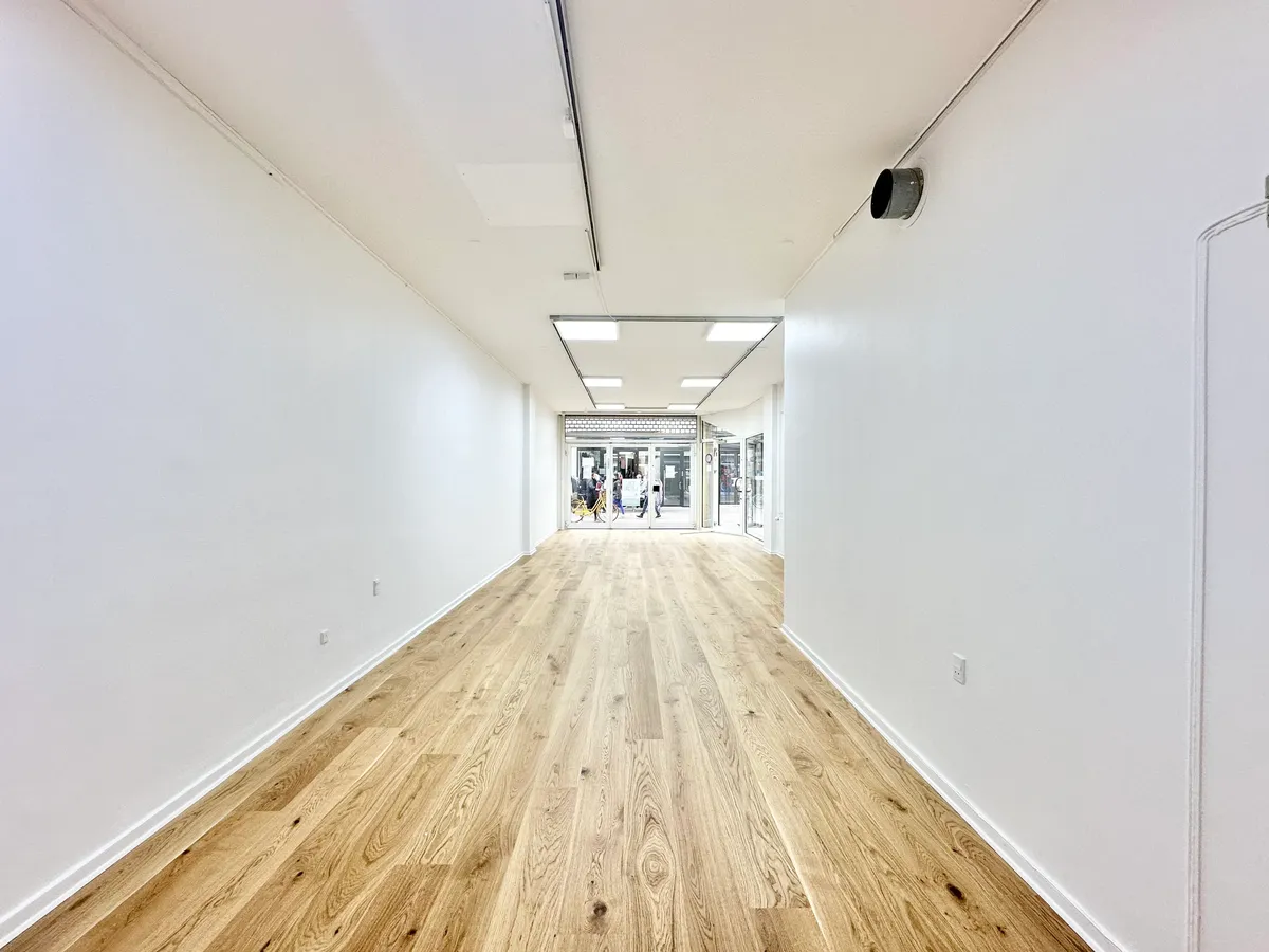 Lej butikslokale med lyse trægulve, hvide vægge og åbne glasdøre til gadefront i Odense centrum. Lejligheden har moderne belysning og er ideel til detaljhandel.