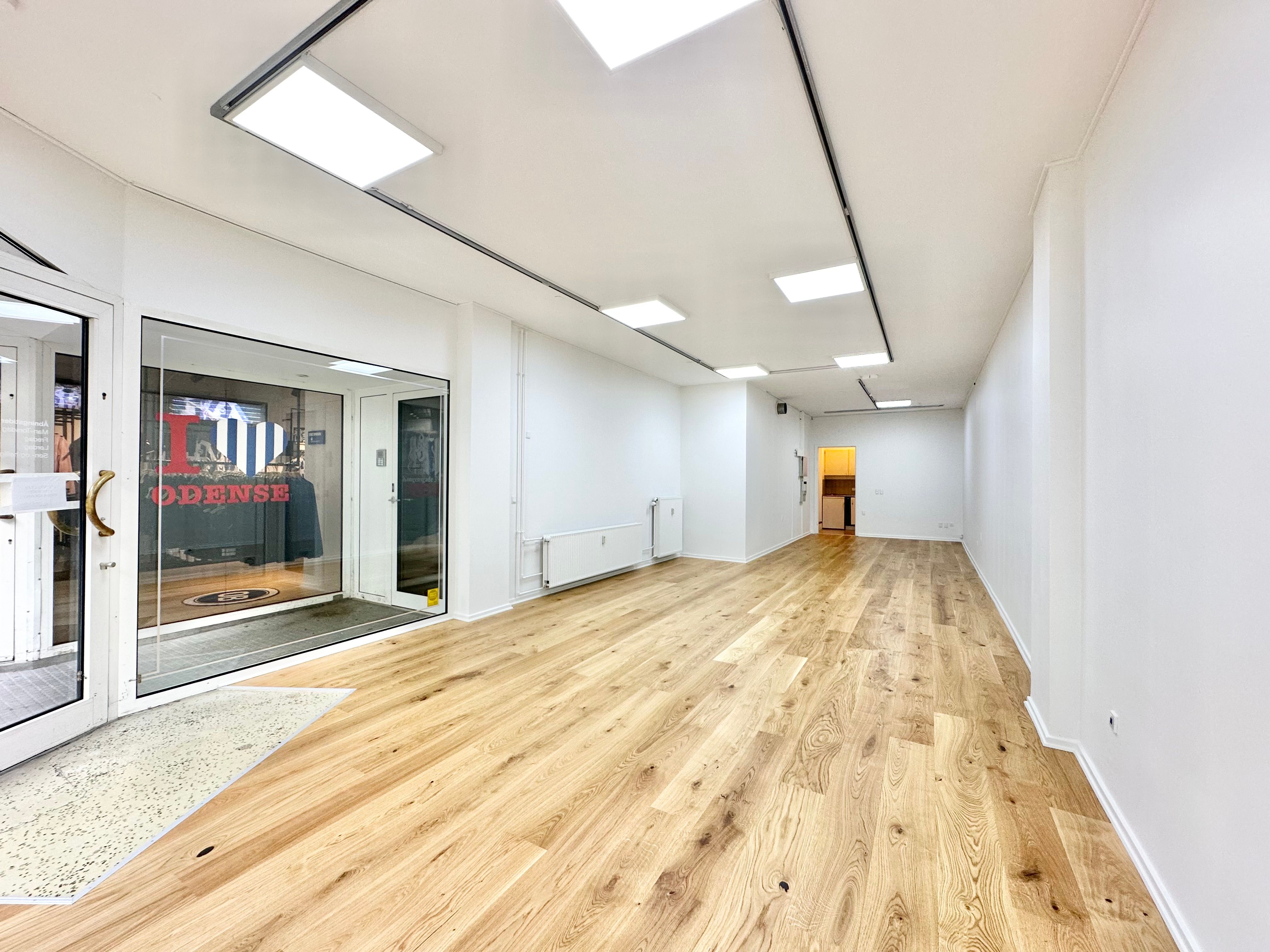 Butik med stort glasvindue og høj lysekron på Kongensgade 39, st. i Odense. Lyst og åbent lokale med lysegulv og flere indgange.