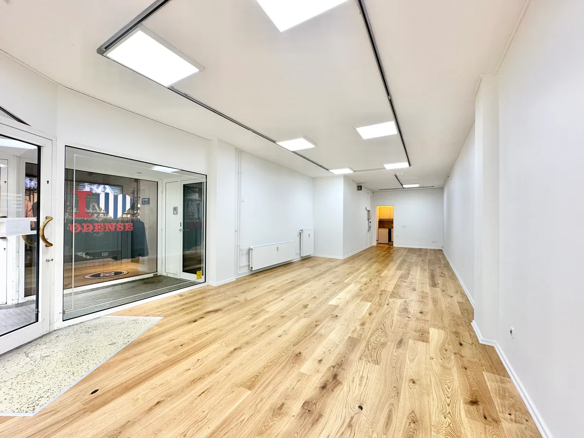 Butik med stort glasvindue og høj lysekron på Kongensgade 39, st. i Odense. Lyst og åbent lokale med lysegulv og flere indgange.