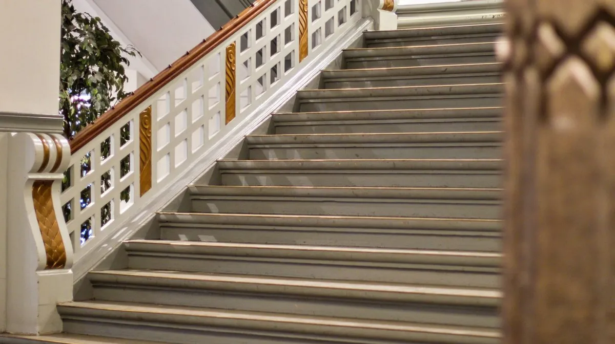 Støbejerns og træ trapper med lyse nuancer og mønstre på siderne. De er placeret indendørs i et hus og har en tydelig