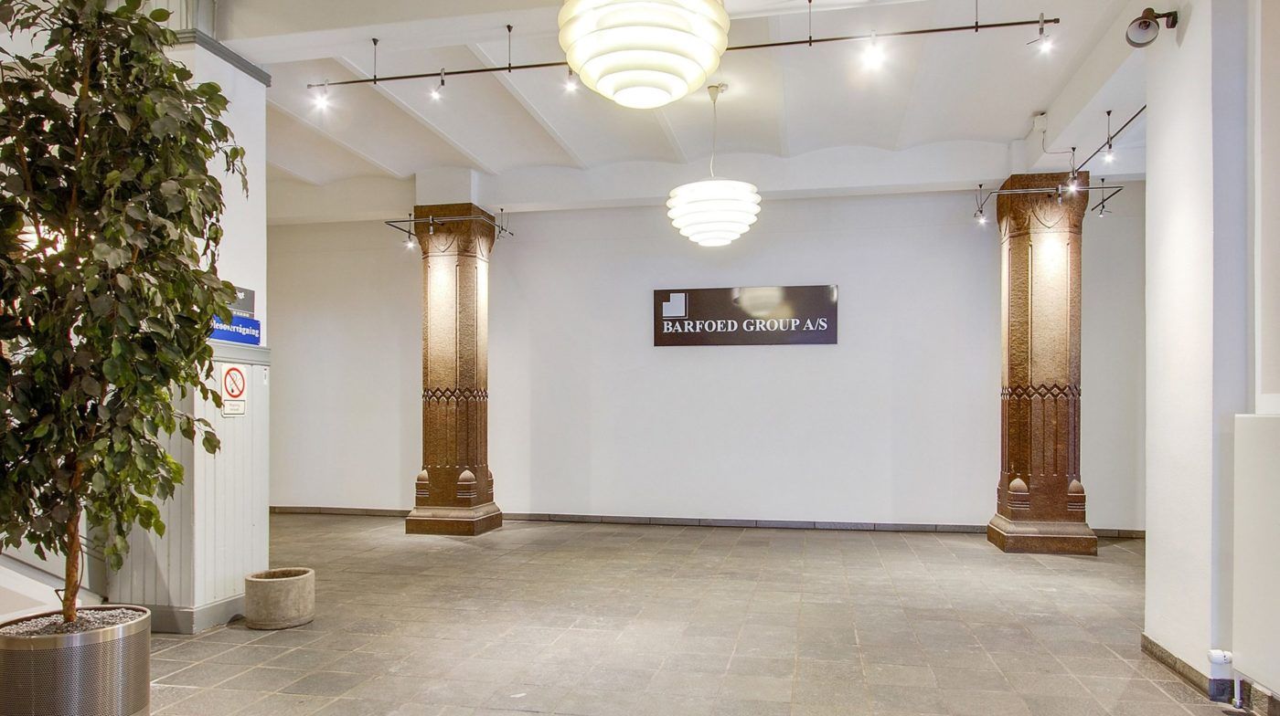 Elegant lobby med højt loft og lysekroner, mønstrede søjler og en stor tekst "BARFOED GROUP A/S" på væggen
