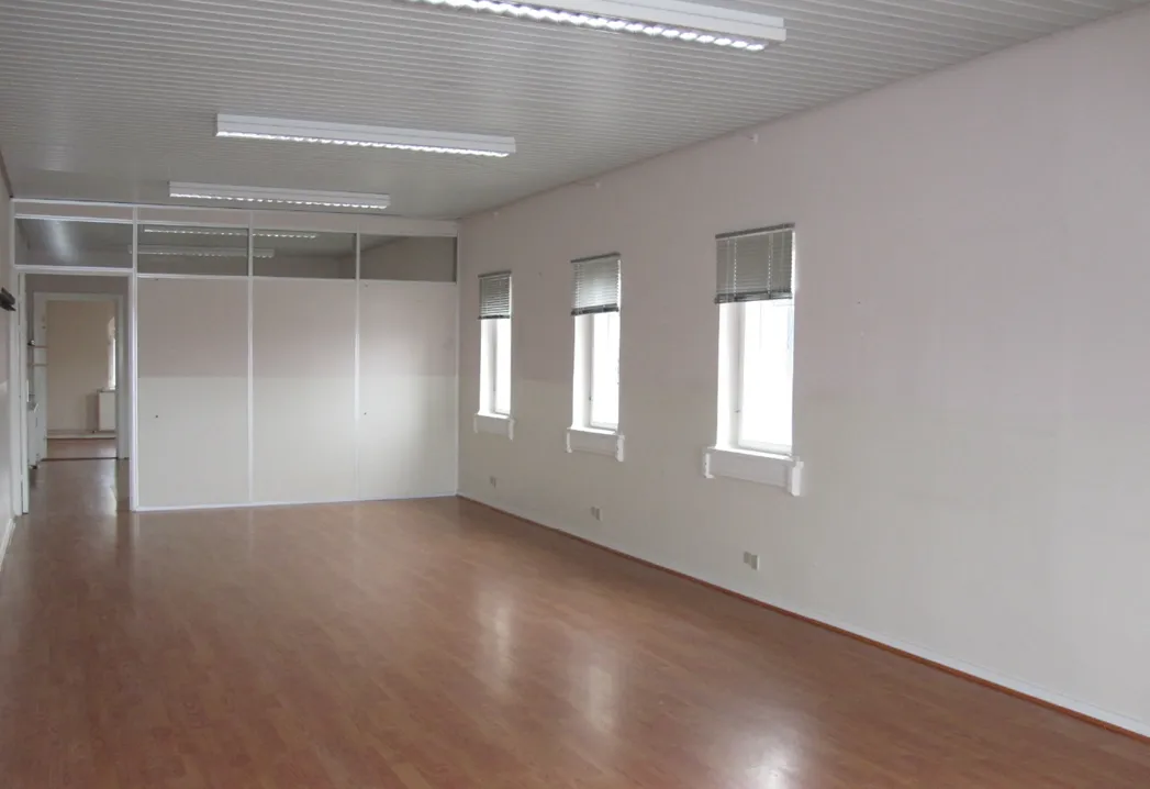 En stor, møbleret, lyse, rummelig stue med 3 vinduer og hvide vægge, en åben dør, højloft og lysegule trægulve.