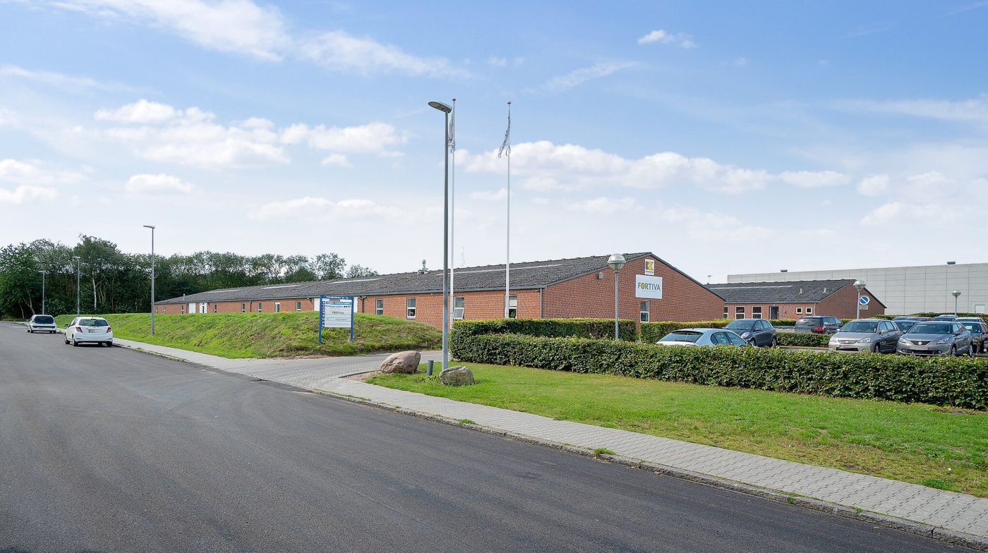 Fabrikstilbygning med Fortviva-skilt og flere parkerede biler i parkeringsplads i Fredericia