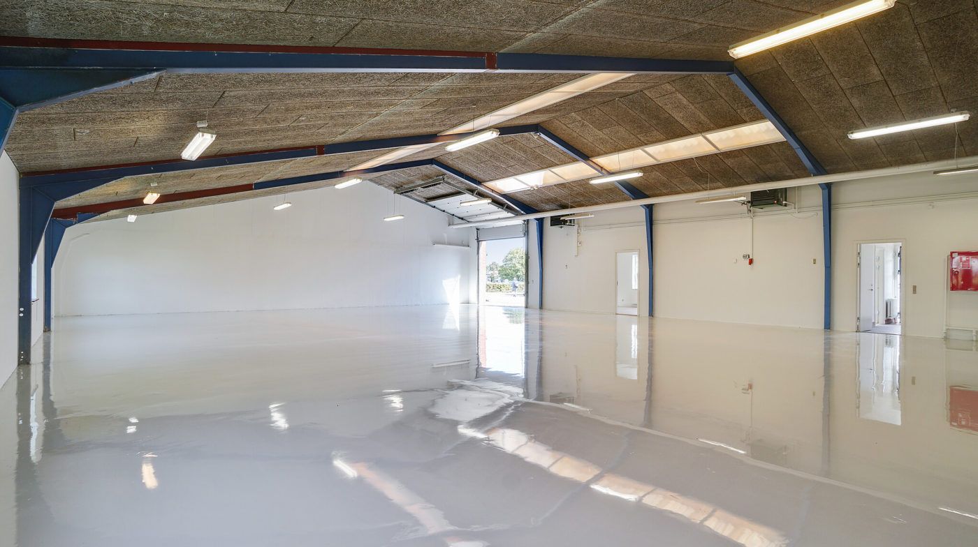 Et stort, nyt lager med hvide vægge og højloft. Der er lysegule striber på loftet, og der er en høj lagerdør i midten