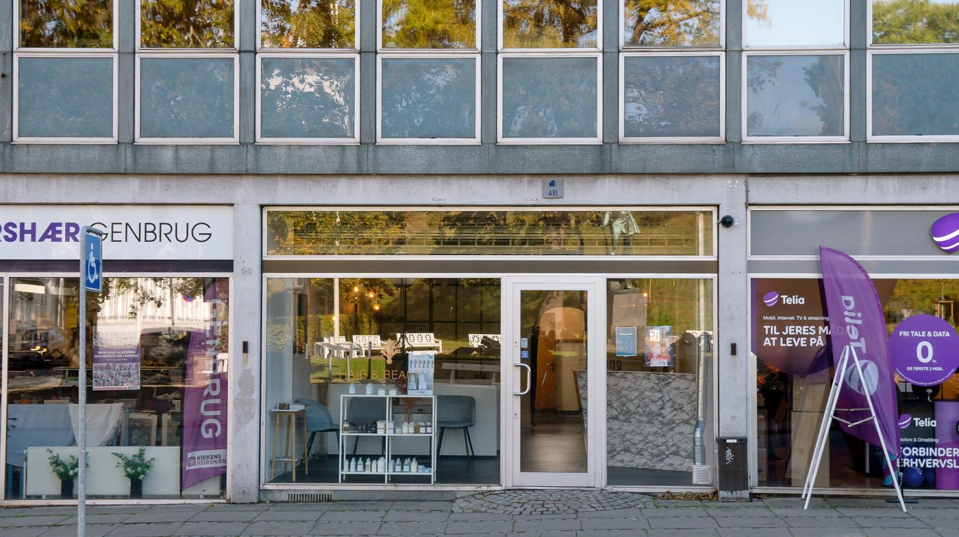 Butiksfront med skilte og reklamebannere, søjle med handicaptegn og Telia-banner samt indvendige butiksvinduer med produkter