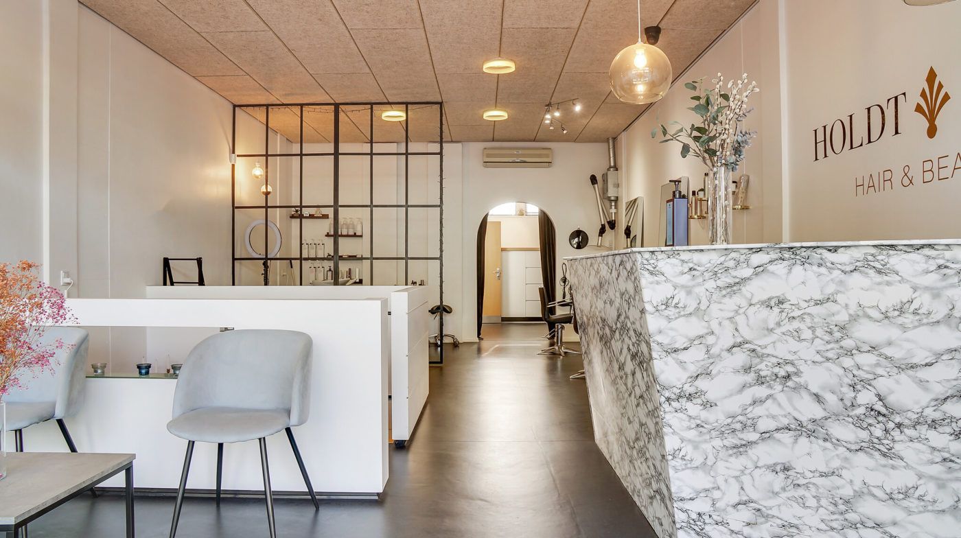 Salon med hårstylingstole og en marmorbar foran et skrift med ordet Holdt