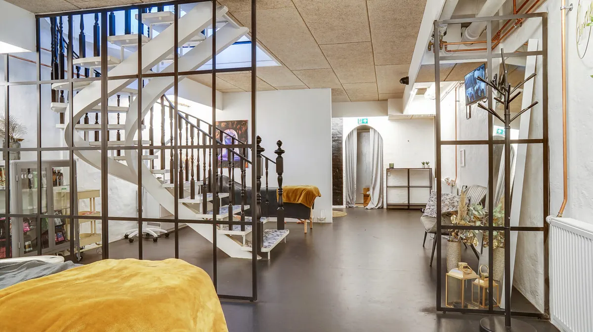 Værelse med dobbeltseng og gult tæppe samt trappe og høj glasdør i hjørnet