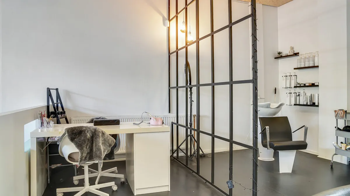 Et moderne sminkeværelse med en hvid stol, et skrivebord, et skraldfad, en hårstol og en hårvask. På væggen er der en høj