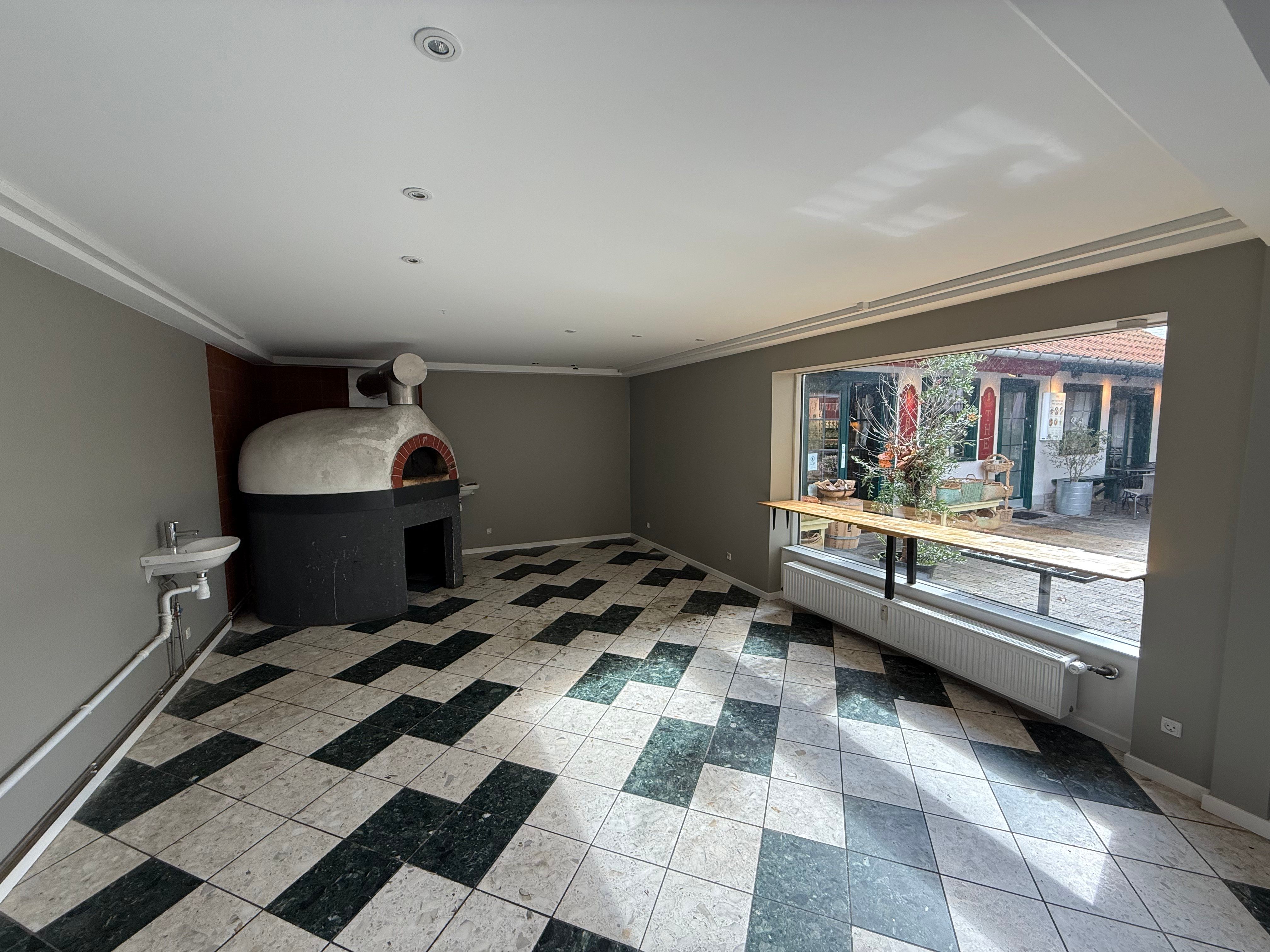 En nydelig, tom værkstedslokal med ovn og en åben vindue til en solrig gårdhave med planter og møbler