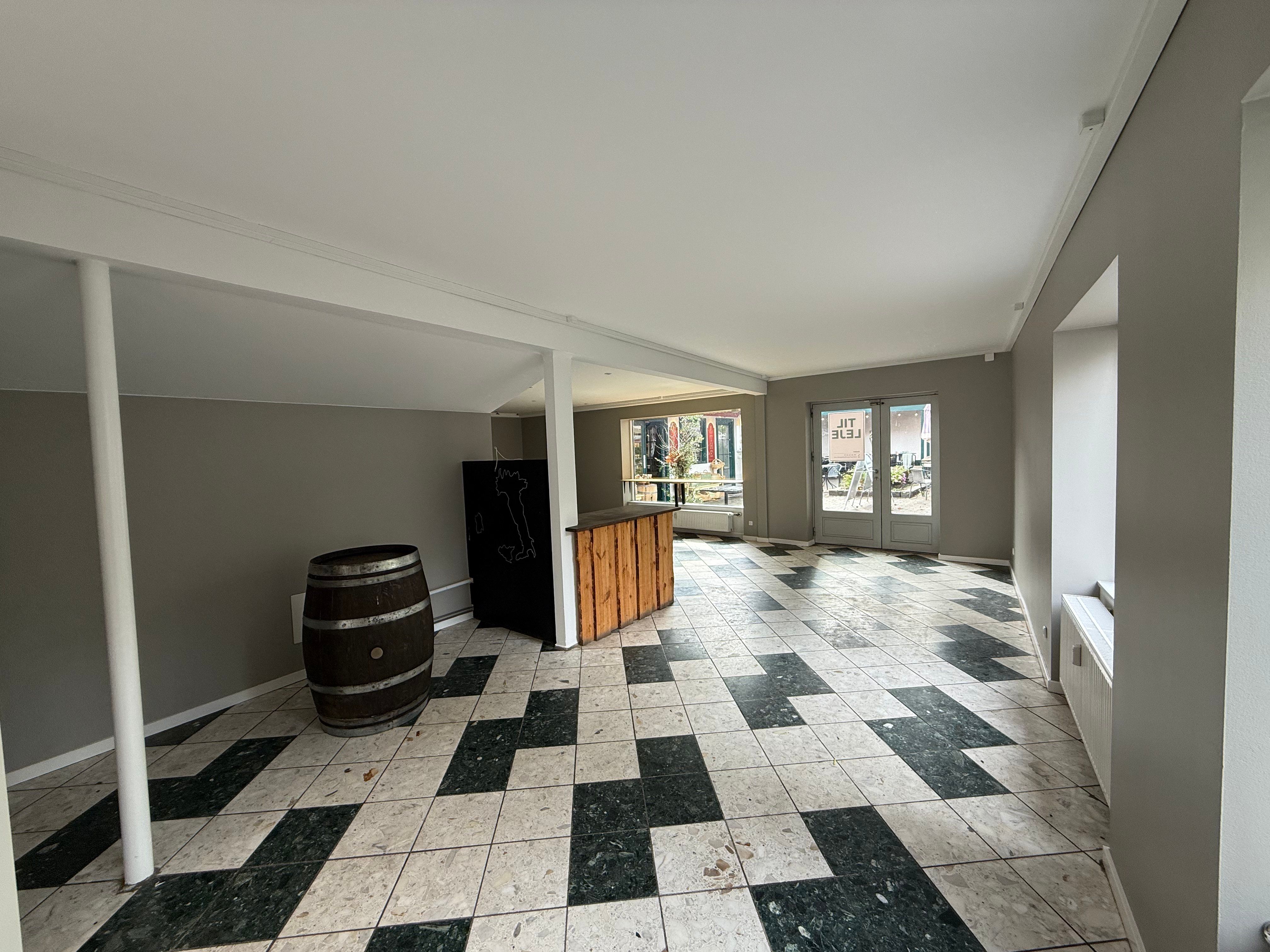 Take-away-lokal med loft, hvidt loft og gulv og træbar. Der er en tønde og en åben dør til udenfor.