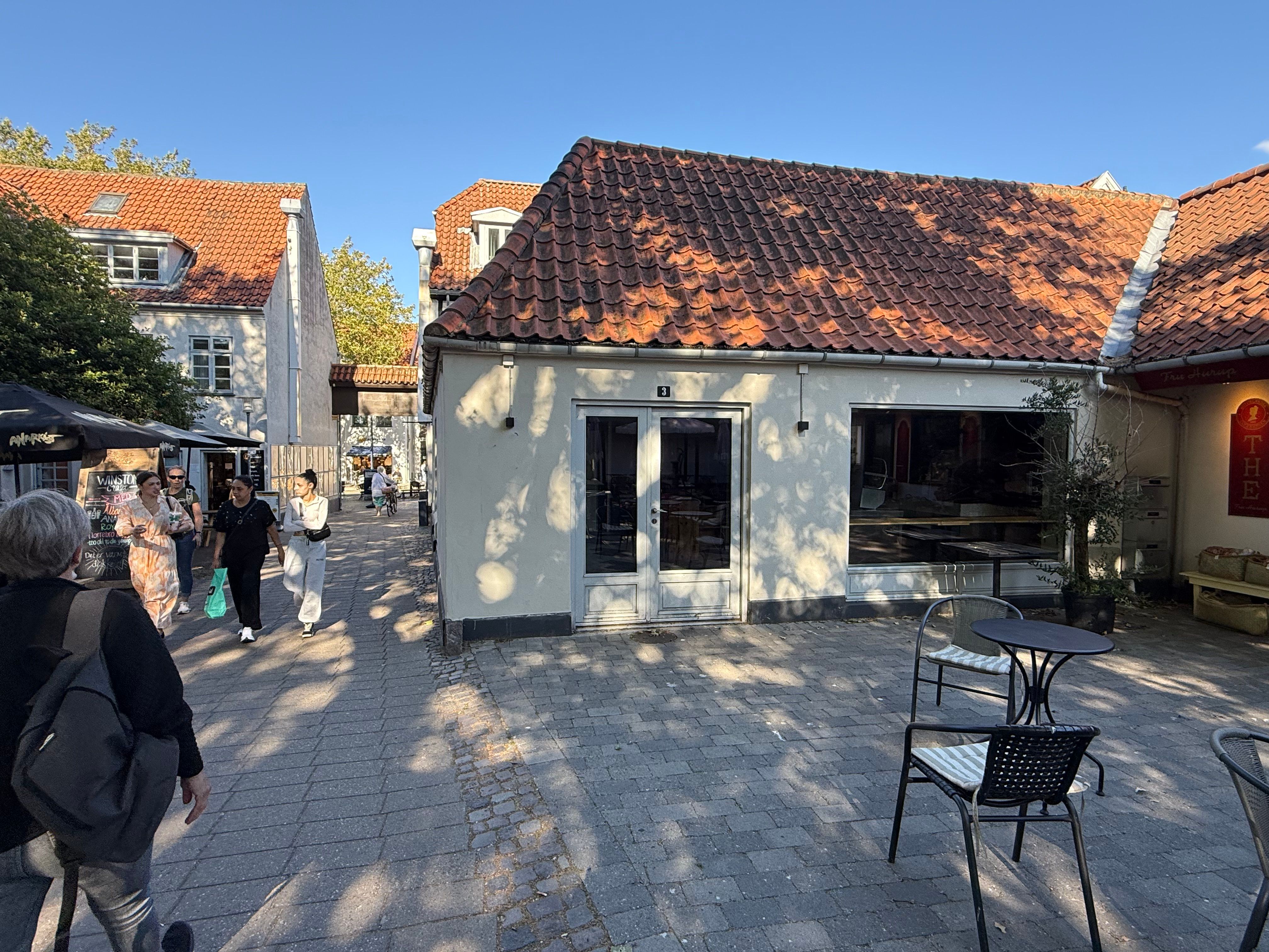 Gæster går forbi caféen med en terrasse og et bord med stole på et gammelt område i Lyngby