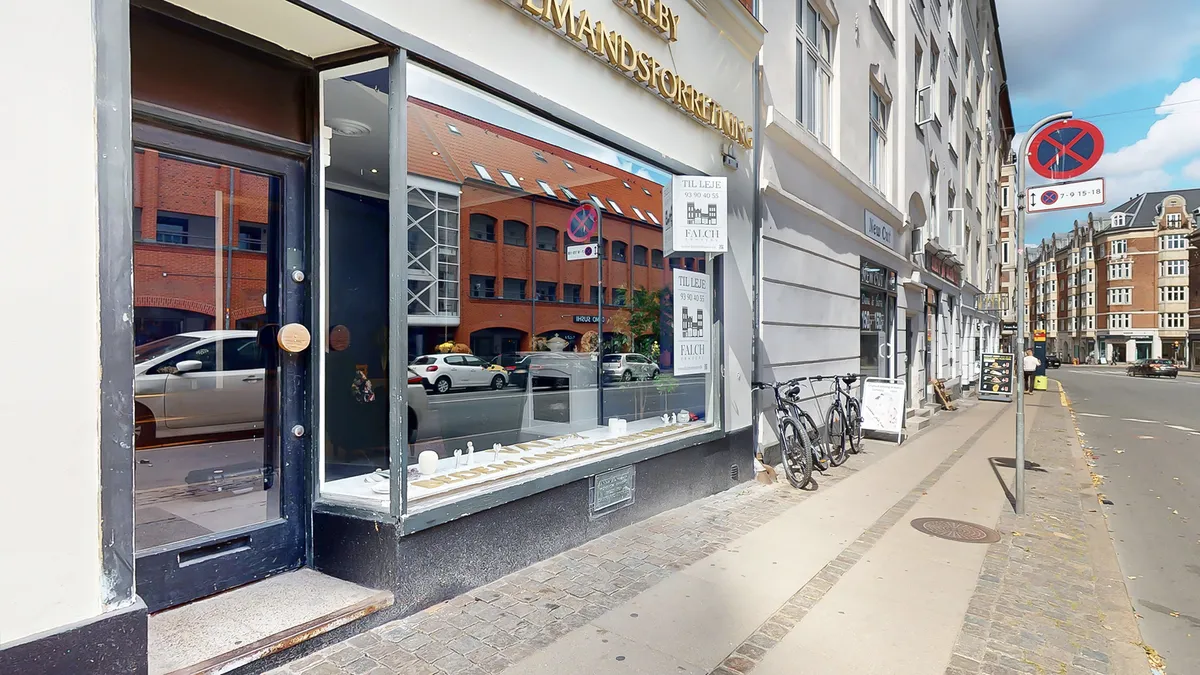 Storefront med vinduer og plakater omkring åbningstider og adresser. To cykler parkeret på siden af gaden og en mand står