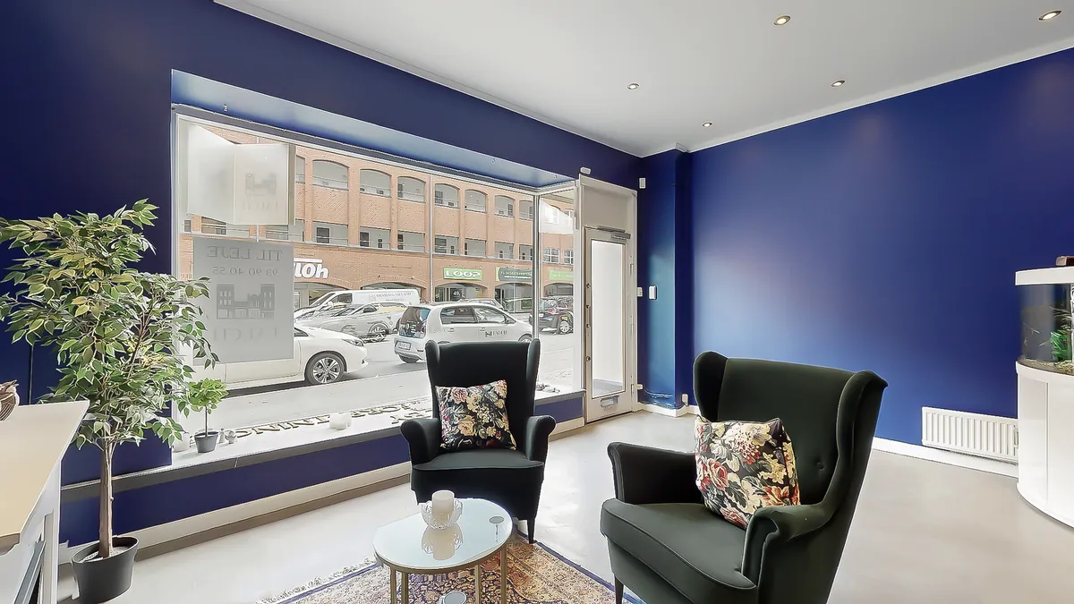 Toftegårds Allé med lyserøde bygninger og parkerede biler, der er udsigt til fra denne lokale i lejemålet. To stole med