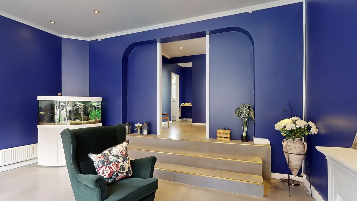 Moderne stue med blå vægge og møbler, en høj gulvlampe og en stor vase med hvide blomster