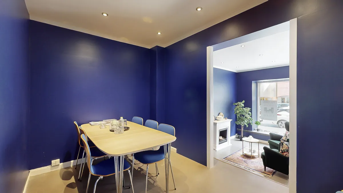 Indvendigt billede af et kontorlokale med blå vægge, lysekroner, runde højstol og moderne møbler i en lyse stue