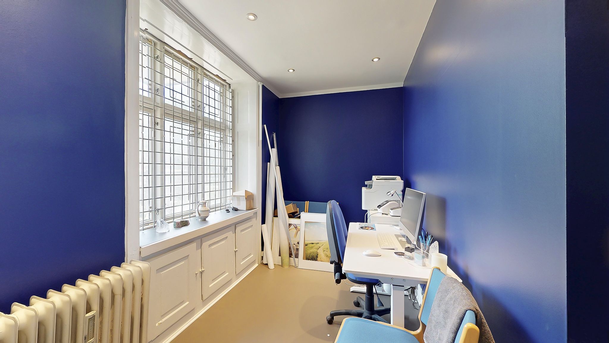 Kontor med computer, skrivebord, stol og klimaanlæg i hjørne med blå vægge og hvide skabe