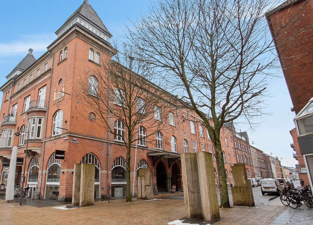 Store røde bygning med flere vinduer og store bueformede indgange og skulpturer på forsiden og et hvidt bord og cykler på