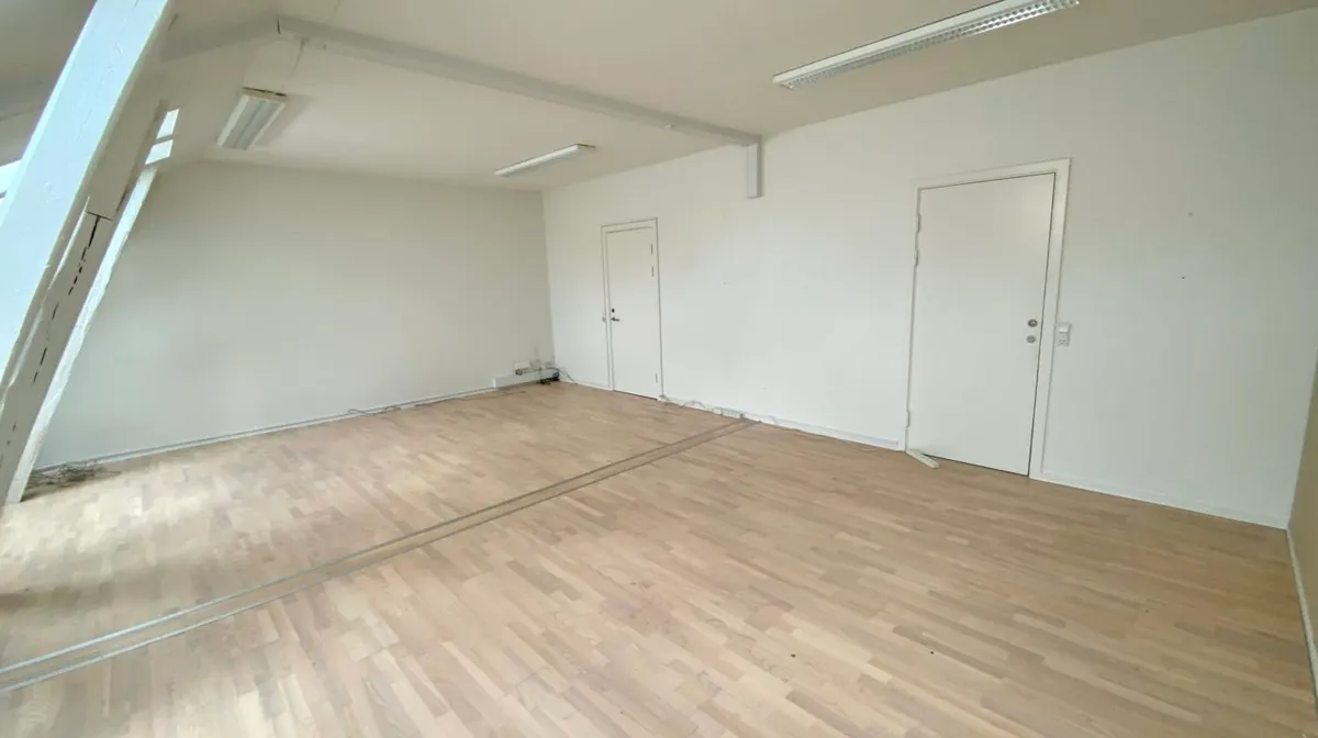 En stor, lys og ren kontor-/showroom med højloft, hvide vægge og trægulve samt to døre og to indbygget lysarmaturer