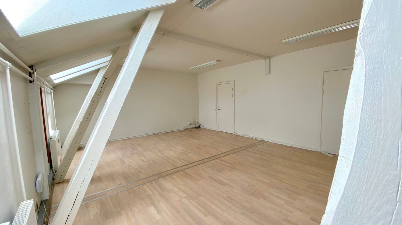 En tom og ren rummelighed med højloft, hvidt loft og vægge samt trægulv og to hvide døre