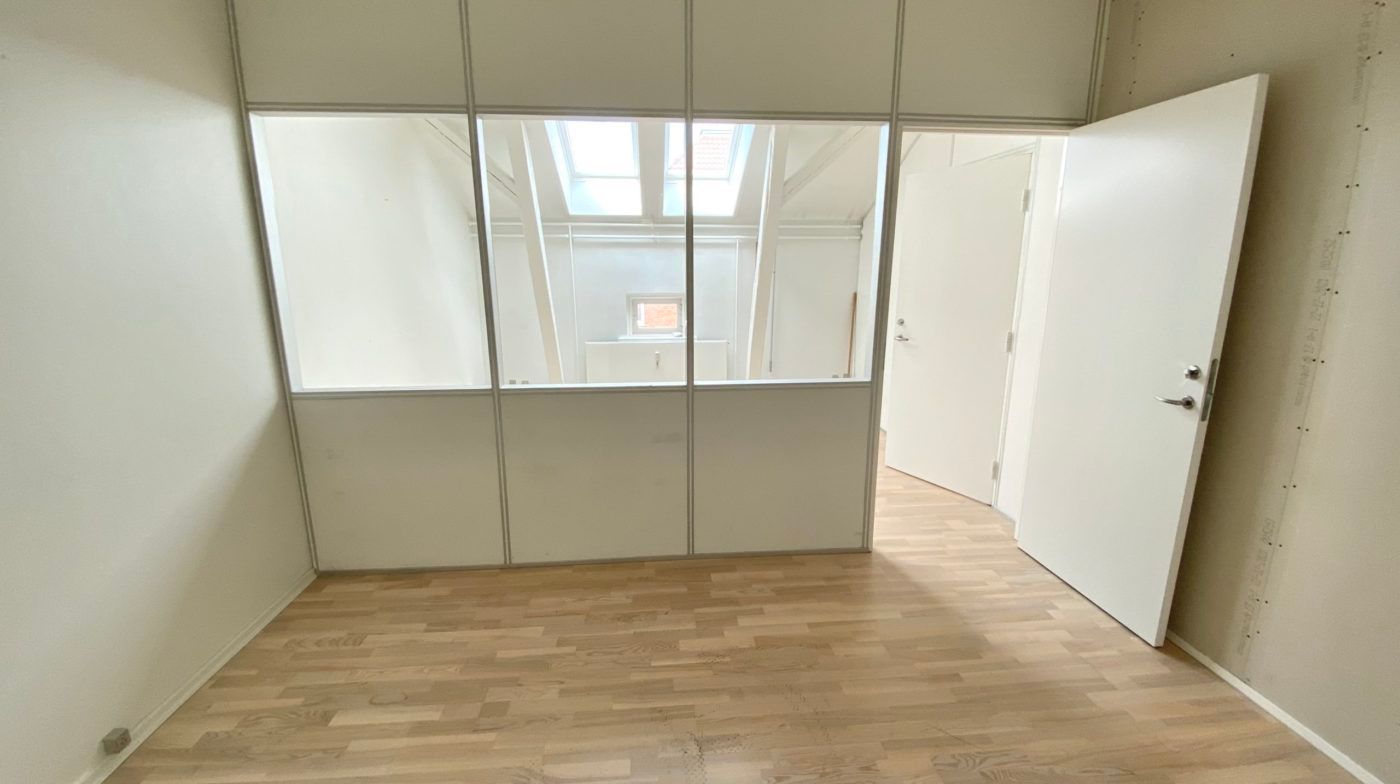 En tom og pænt indrettet kontor- eller showroom med trægulv, hvide vægge og glasvinduer, der ud til en åben dør