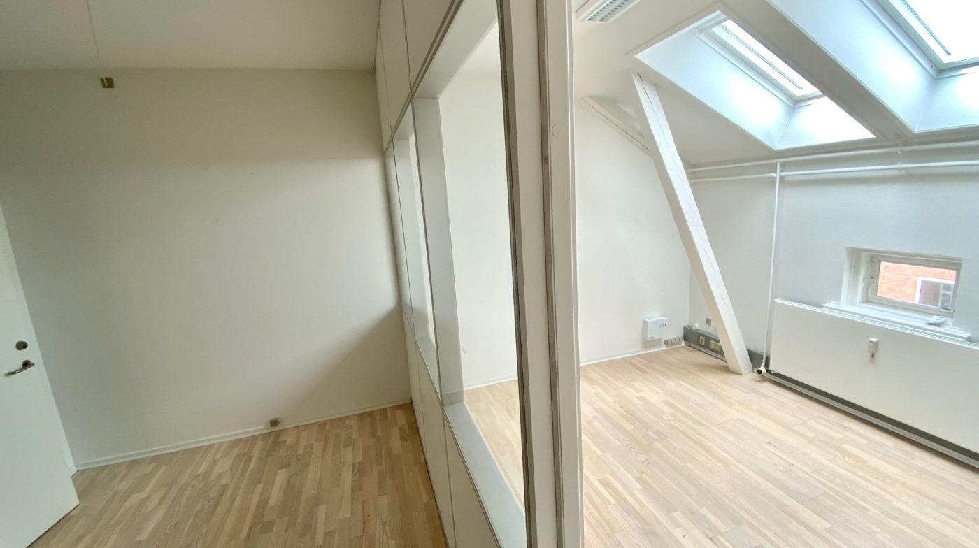 En stor åben stue med højt til loftet, loftsvinduer, lysegulve og hvide vægge. Et hvidt radiator er placeret ved siden af