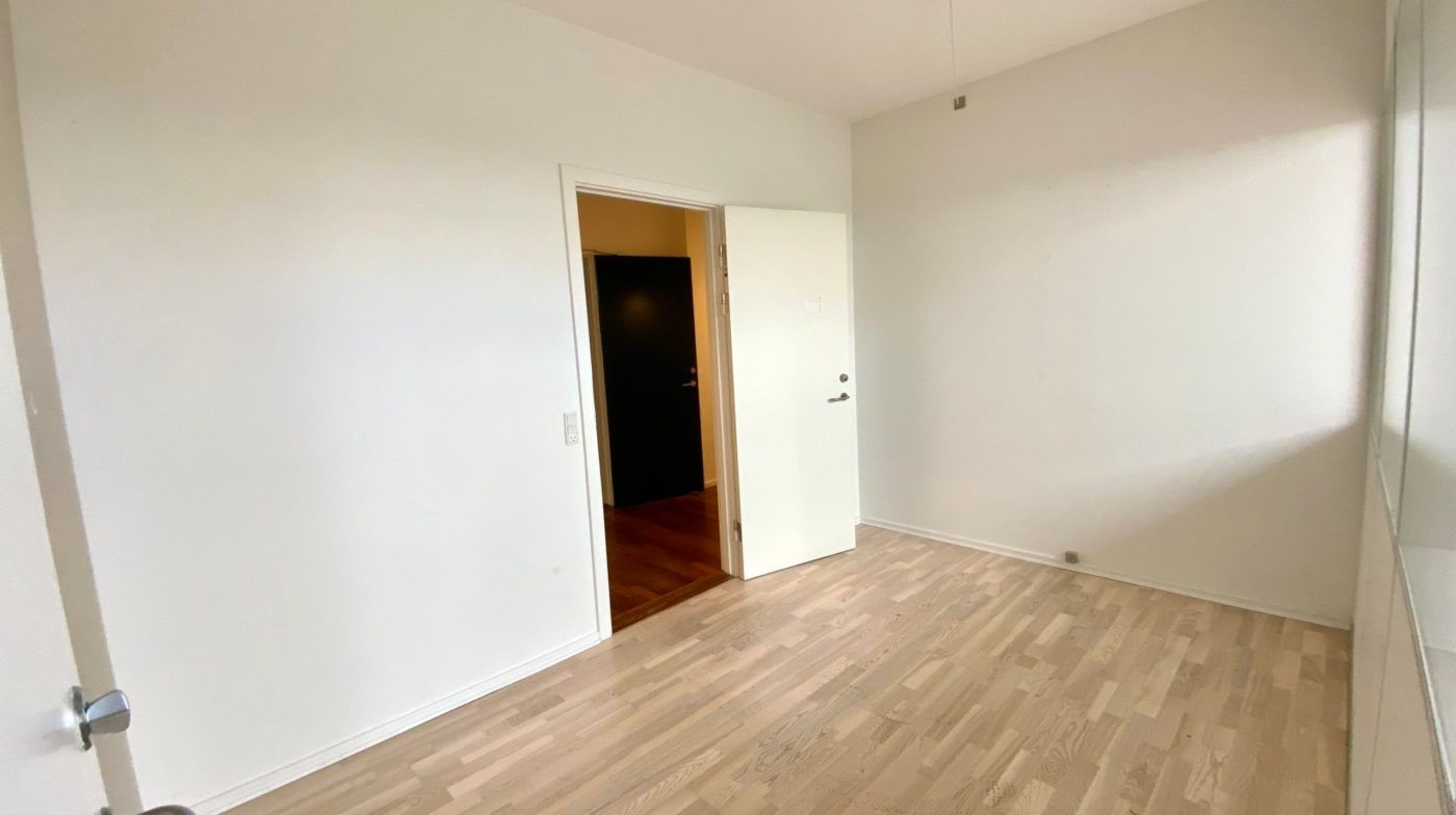 Et moderne og rent værelse med hvide vægge, hårdt trægulv og to døre, en åben og en lukket, foran en glasvæg