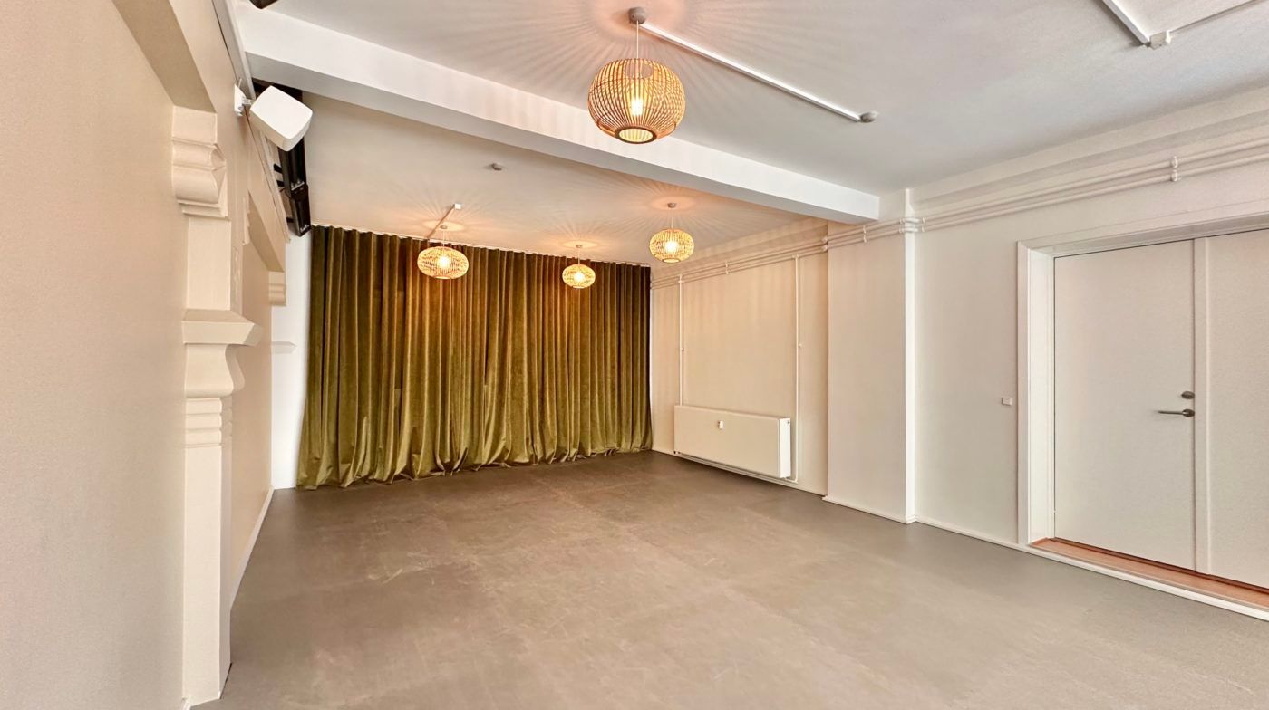 En stor, ren og lys hall med hvide vægge og loft, lyse gulvbelægning, tre hængelampe og en stor gardin, samt dør til et