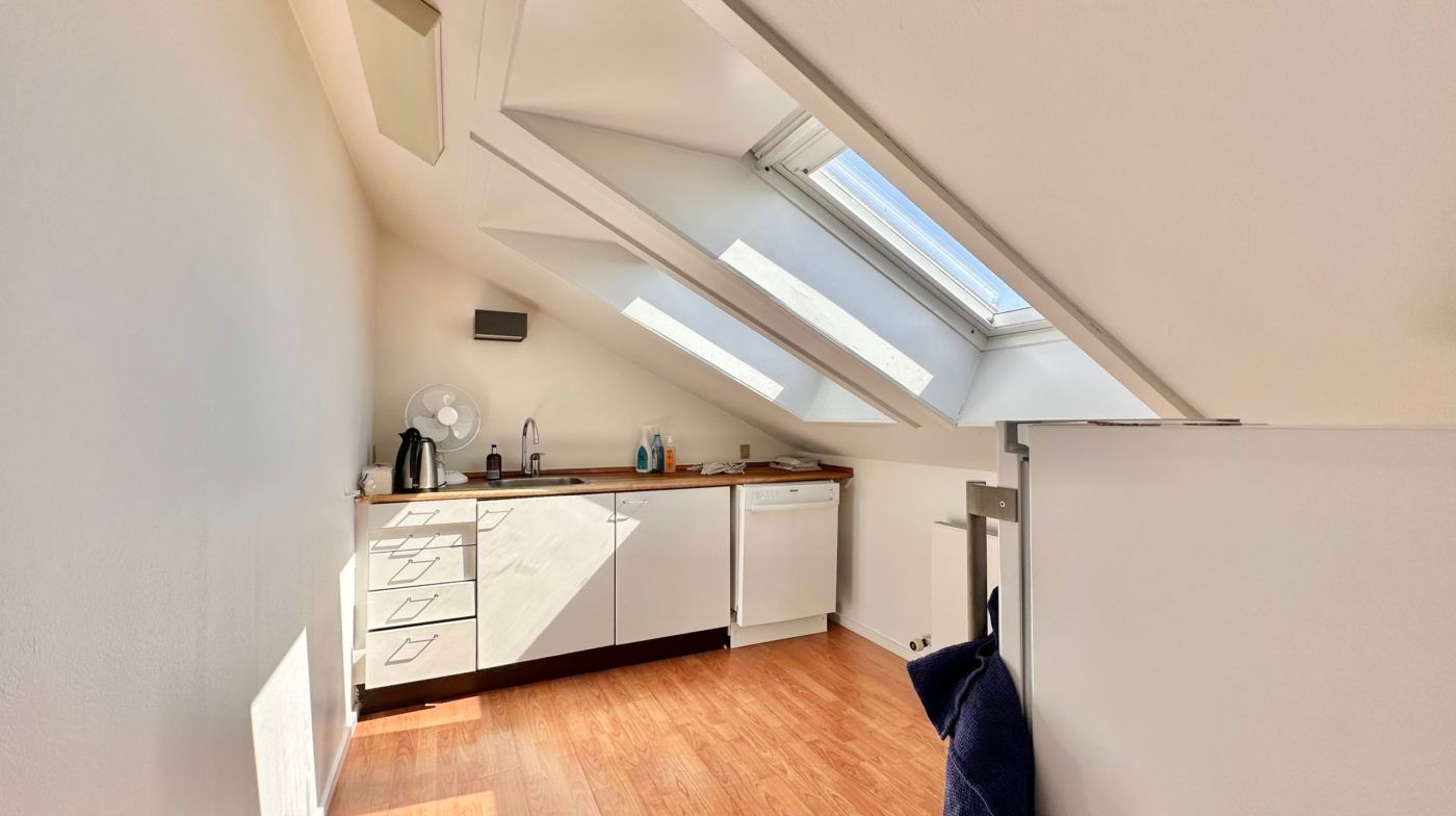 Loftsværelse med loftsvindue, hvide vægge, hvide skabe, køkkenapparater og en børste i loftet