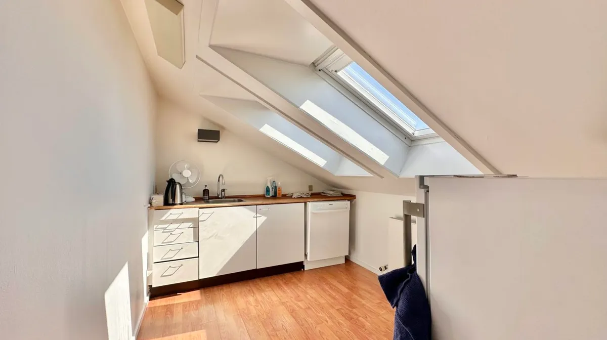 Loftsværelse med loftsvindue, hvide vægge, hvide skabe, køkkenapparater og en børste i loftet