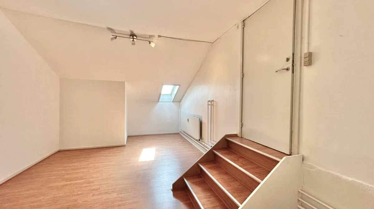 Lokaler med åbne lofter og vinduesindbygget lys. Sti med trætrin og hvid væg med dør og elektriske stikkontakter