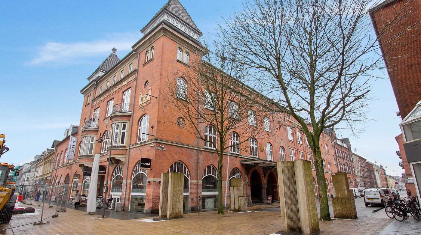 En stor rødmaursten bygning med mange vinduer og en skrånende tagkontur, samt FinForm Fitness skilt og gulvudsmykninger