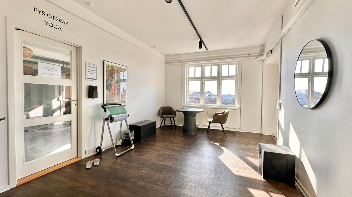 Lokaler med møbler og fitnessudstyr. To stole og et bord samt en rund spejl og hængende lys.