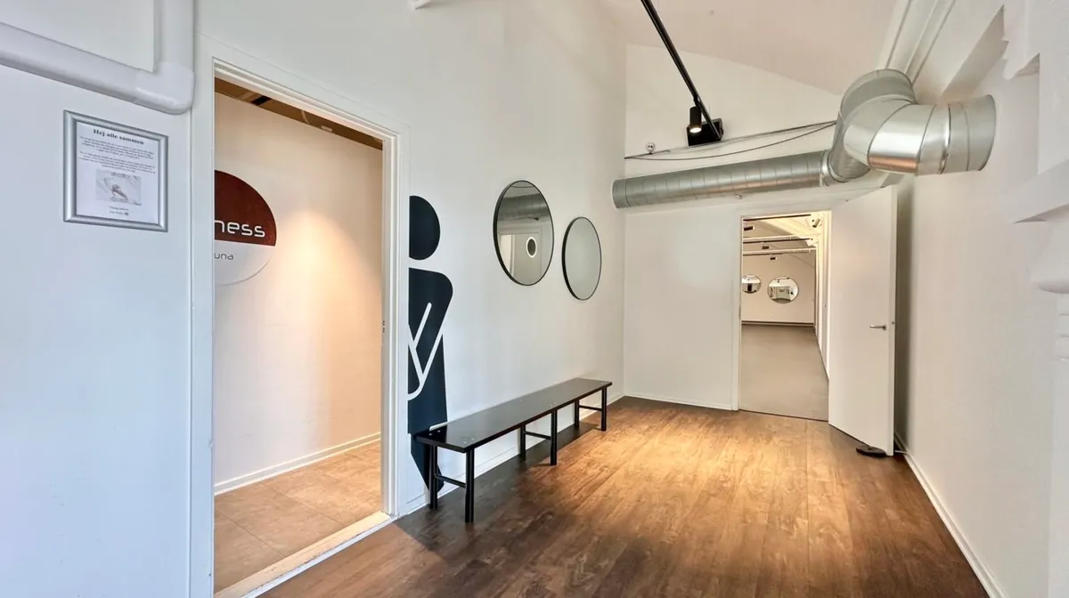 Et rensedes, minimalistiskt designet lokale med tre spejle og en tavle på væggen. To døre er åbne, og en længdebord og en